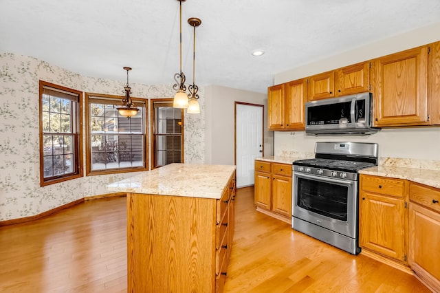 kitchen with light stone counters, stainless steel appliances, decorative light fixtures, light hardwood / wood-style floors, and a kitchen island