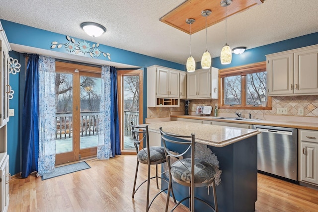 kitchen featuring decorative light fixtures, a textured ceiling, a kitchen island, stainless steel dishwasher, and sink