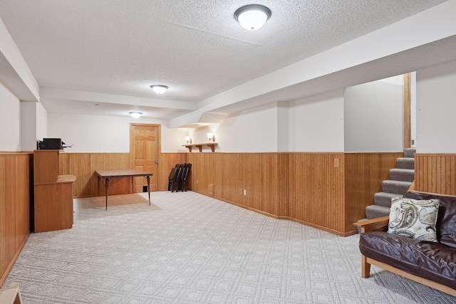 interior space featuring a textured ceiling, light colored carpet, and wood walls