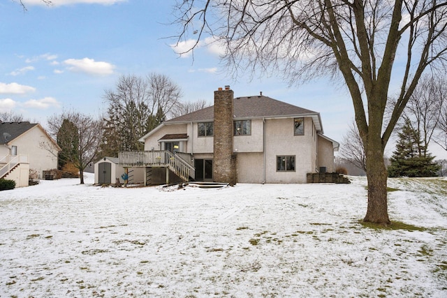 snow covered back of property featuring a deck and a shed