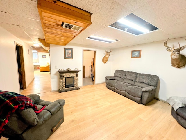 living room featuring hardwood / wood-style flooring, a stone fireplace, and a paneled ceiling