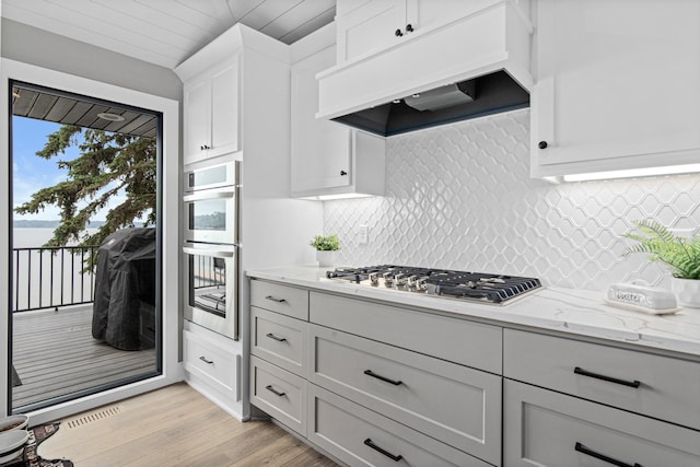 804 County Road I W, Shoreview, MN 55126 - kitchen with appliances with stainless steel finishes, under cabinet range hood, light stone countertops, light wood-style floors, and decorative backsplash