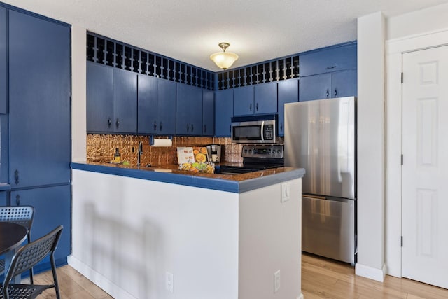 kitchen with blue cabinets, dark countertops, stainless steel appliances, a peninsula, and light wood finished floors