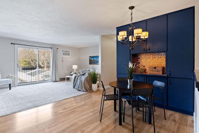 dining room with an AC wall unit, a textured ceiling, light wood-style floors, baseboards, and a chandelier