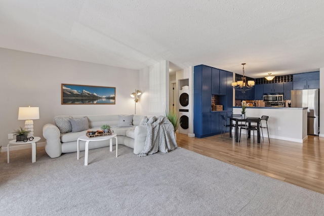 living area with a textured ceiling, light wood-type flooring, stacked washer / drying machine, and a chandelier