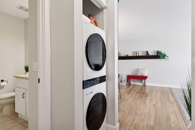 laundry area featuring visible vents, light wood-style flooring, laundry area, and stacked washing maching and dryer