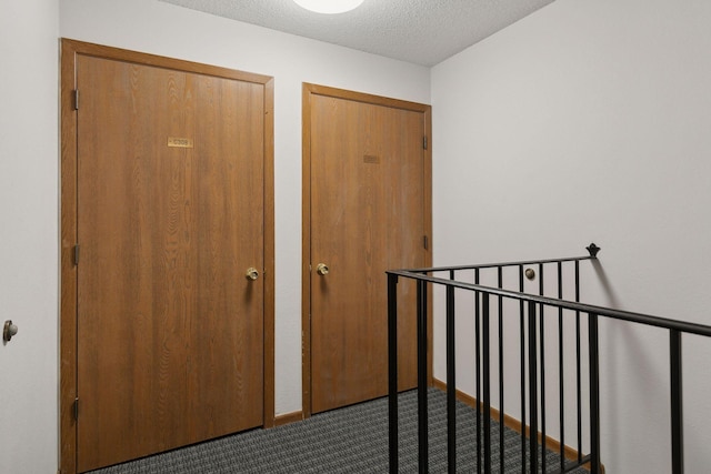 hall with dark carpet, a textured ceiling, and baseboards