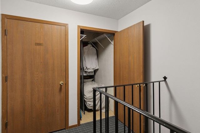 hallway with an upstairs landing, carpet floors, and a textured ceiling