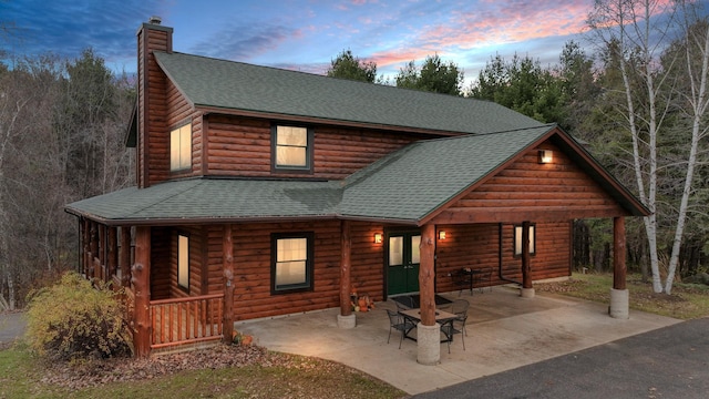 18059 County Highway Oo, Chippewa Falls, WI 54729 - view of front of house with roof with shingles, a chimney, covered porch, log veneer siding, and a patio