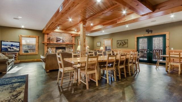 dining area with beam ceiling, a stone fireplace, wood ceiling, and french doors