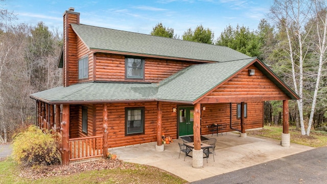 18059 County Highway Oo, Chippewa Falls, WI 54729 - view of front of house featuring a shingled roof, a chimney, faux log siding, covered porch, and a patio area