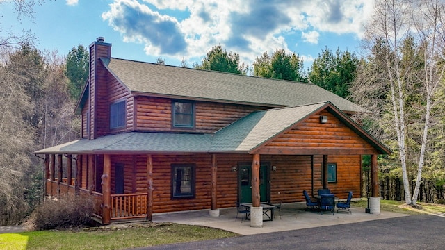 cabin with a porch, a chimney, faux log siding, and roof with shingles