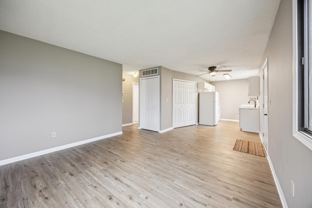 unfurnished living room featuring a textured ceiling, light hardwood / wood-style floors, ceiling fan, and sink