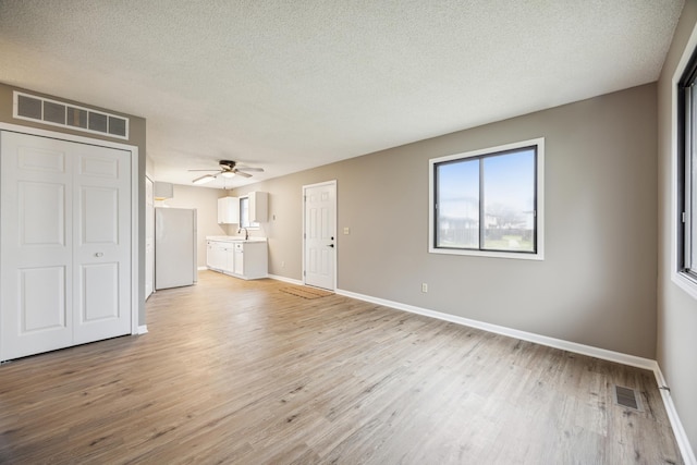 unfurnished living room featuring ceiling fan, a textured ceiling, and light hardwood / wood-style flooring