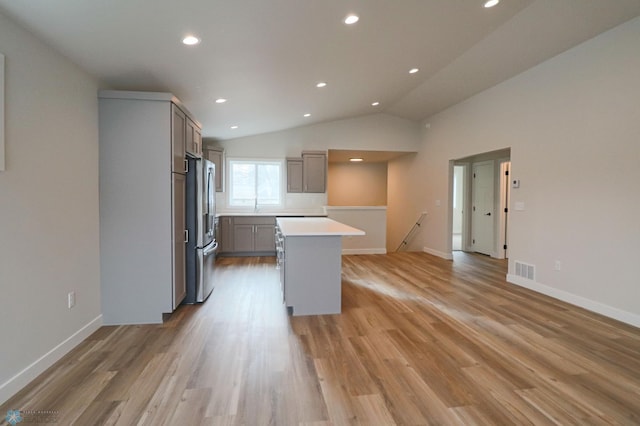 kitchen with gray cabinetry, a center island, lofted ceiling, light wood-type flooring, and stainless steel refrigerator