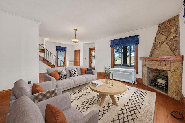 living room featuring a stone fireplace, wood-type flooring, and radiator heating unit