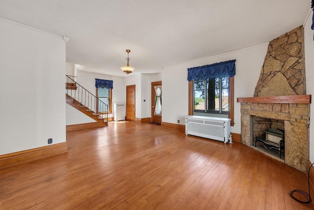 unfurnished living room with radiator, a stone fireplace, and wood-type flooring