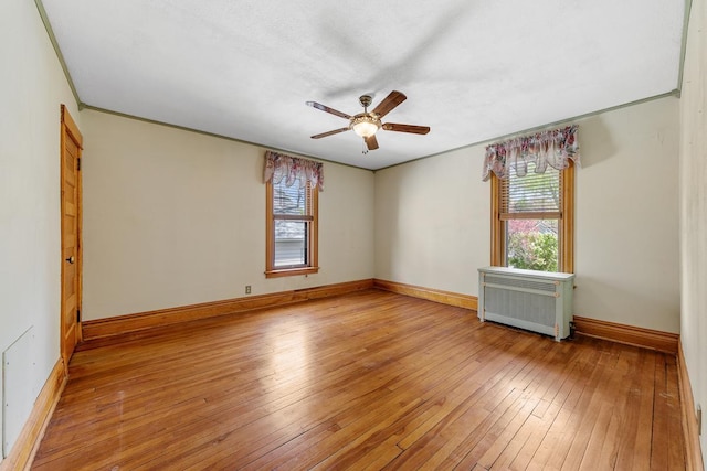 empty room with radiator, a wealth of natural light, ceiling fan, and light wood-type flooring