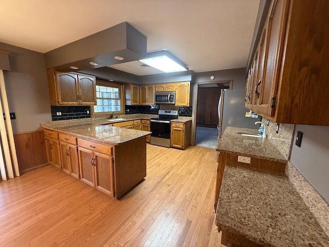 kitchen with kitchen peninsula, appliances with stainless steel finishes, light hardwood / wood-style floors, and sink