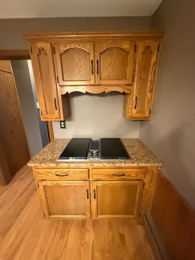 kitchen featuring black electric cooktop, light stone counters, and light hardwood / wood-style flooring