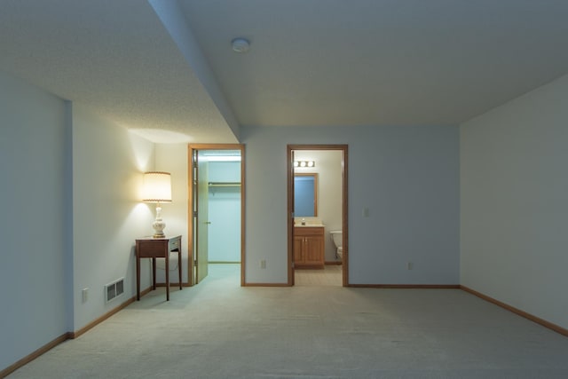 bedroom featuring light carpet, ensuite bath, a textured ceiling, a spacious closet, and a closet