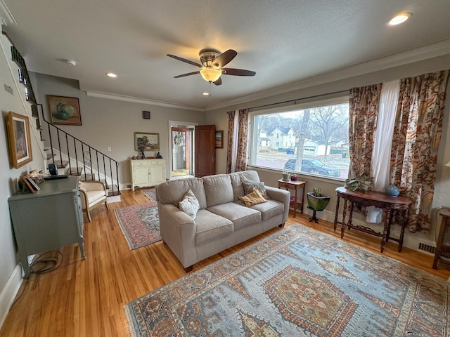 living room with a textured ceiling, light hardwood / wood-style flooring, ceiling fan, and crown molding