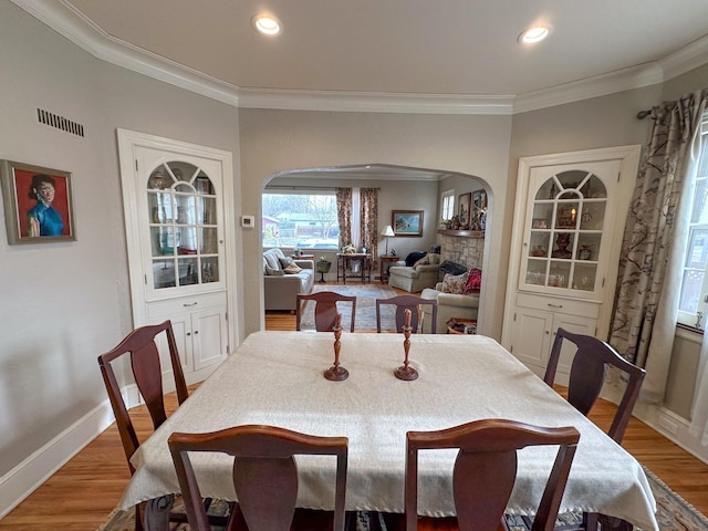 dining area with a stone fireplace, wood-type flooring, and crown molding