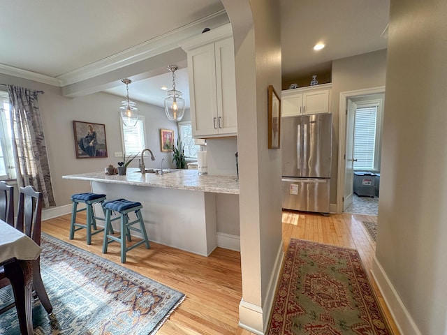 kitchen featuring white cabinets, stainless steel fridge, light wood-type flooring, and a kitchen bar