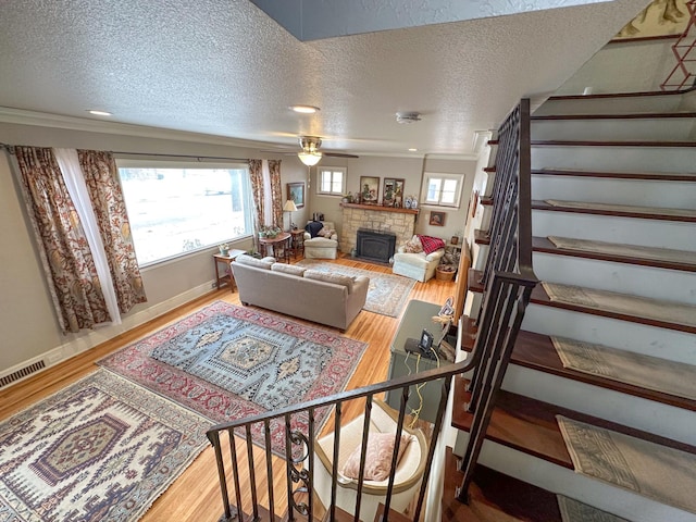 living room featuring hardwood / wood-style flooring, crown molding, a stone fireplace, and a textured ceiling