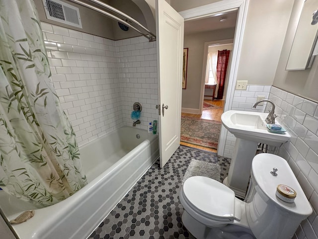 bathroom featuring shower / bath combination with curtain, toilet, and tile walls