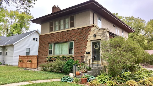 view of front of property with stucco siding, a chimney, a front lawn, and brick siding