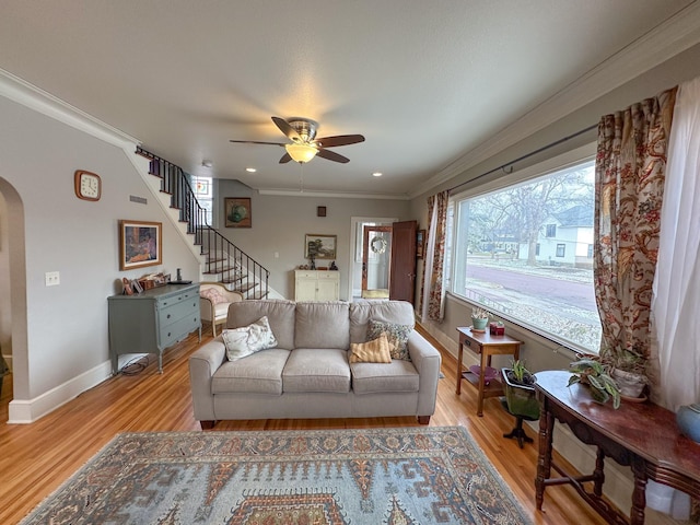 living area with ceiling fan, arched walkways, ornamental molding, light wood finished floors, and baseboards