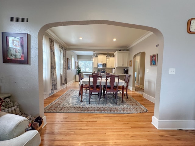dining space featuring ornamental molding, arched walkways, light wood-style flooring, baseboards, and recessed lighting
