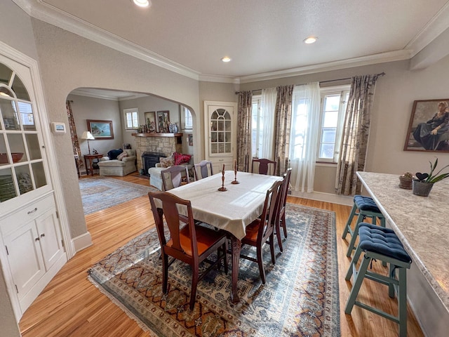 dining area featuring arched walkways, a fireplace, ornamental molding, light wood-style flooring, and recessed lighting