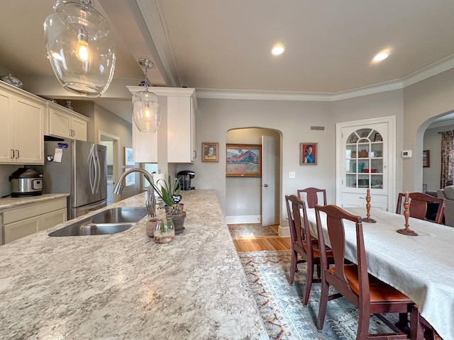 kitchen featuring arched walkways, a sink, freestanding refrigerator, light countertops, and ornamental molding