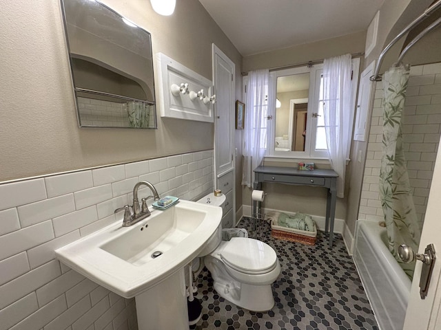 full bathroom featuring toilet, shower / tub combo with curtain, tile walls, and wainscoting