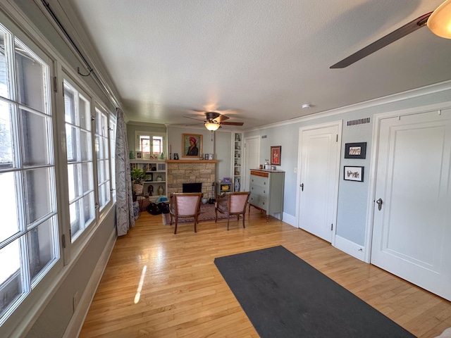 workout area with ceiling fan, a textured ceiling, light wood finished floors, a stone fireplace, and baseboards