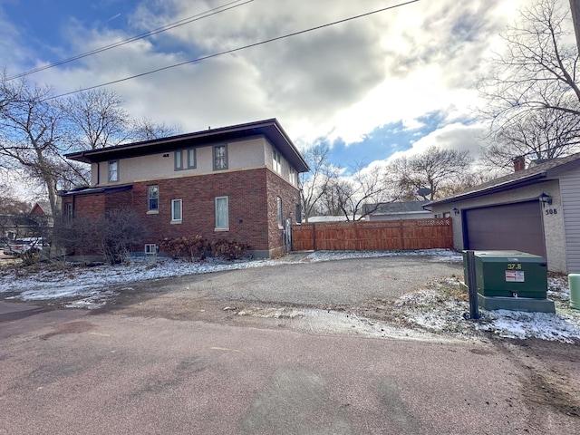 view of snow covered exterior with brick siding, fence, and asphalt driveway