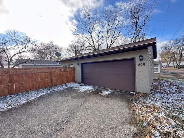 snow covered garage with asphalt driveway and fence