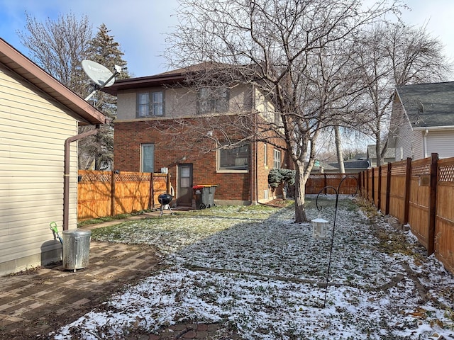 snow covered property featuring brick siding and a fenced backyard