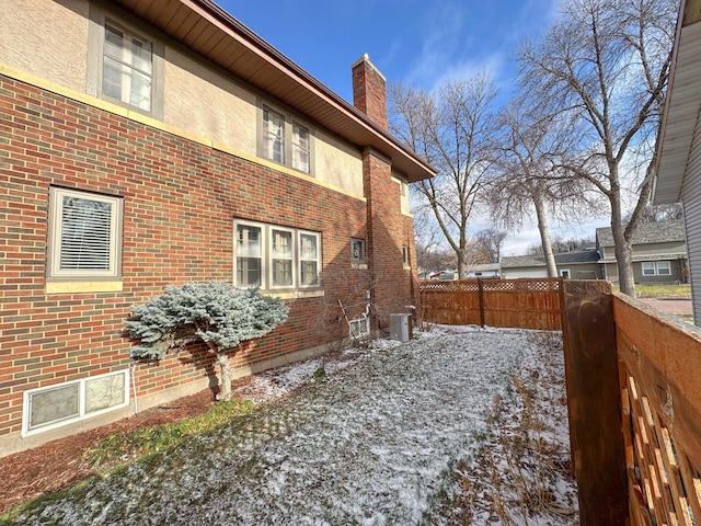 view of home's exterior featuring fence, brick siding, a chimney, and cooling unit