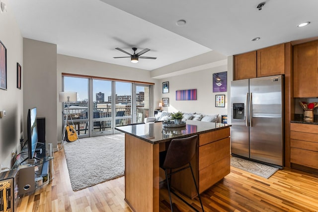 kitchen featuring a breakfast bar area, light wood-type flooring, dark stone countertops, stainless steel fridge, and a kitchen island