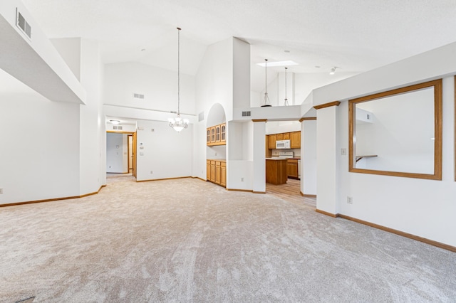 unfurnished living room with visible vents, baseboards, high vaulted ceiling, light colored carpet, and a chandelier