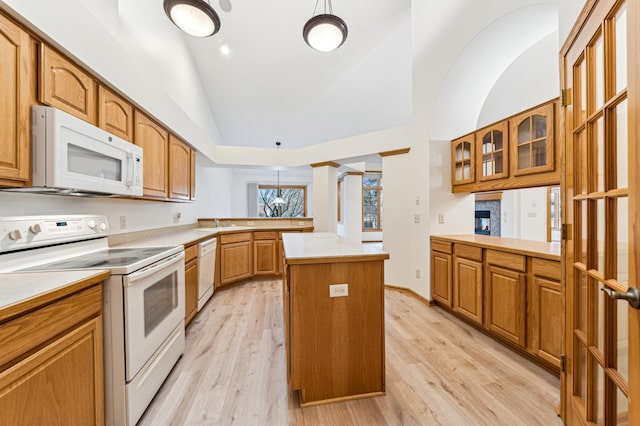 kitchen featuring a kitchen island, light countertops, vaulted ceiling, a peninsula, and white appliances