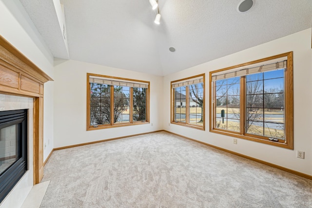 unfurnished living room with baseboards, vaulted ceiling, light carpet, a glass covered fireplace, and a textured ceiling