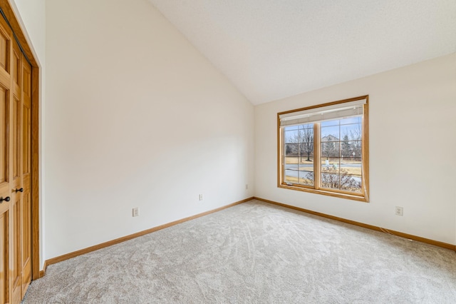 unfurnished room featuring vaulted ceiling, light colored carpet, and baseboards