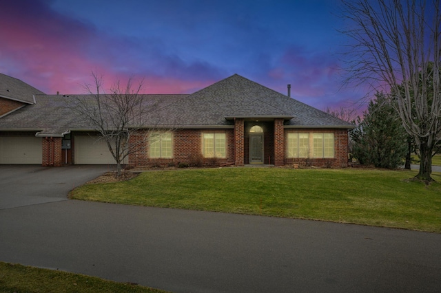 ranch-style house featuring brick siding, roof with shingles, driveway, a yard, and an attached garage