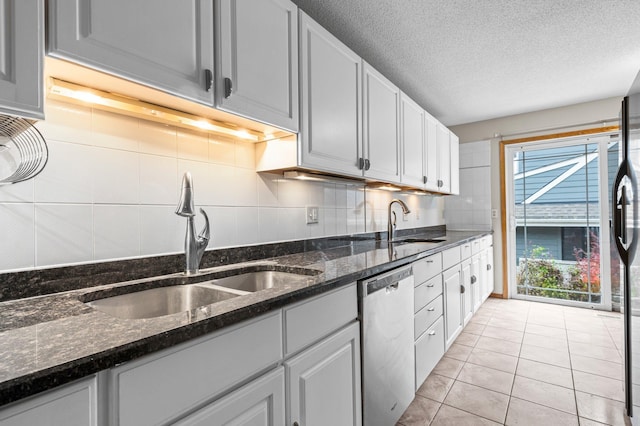 kitchen featuring backsplash, dark stone counters, sink, dishwasher, and light tile patterned flooring