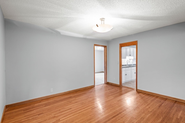 empty room with a textured ceiling, light wood-type flooring, and sink