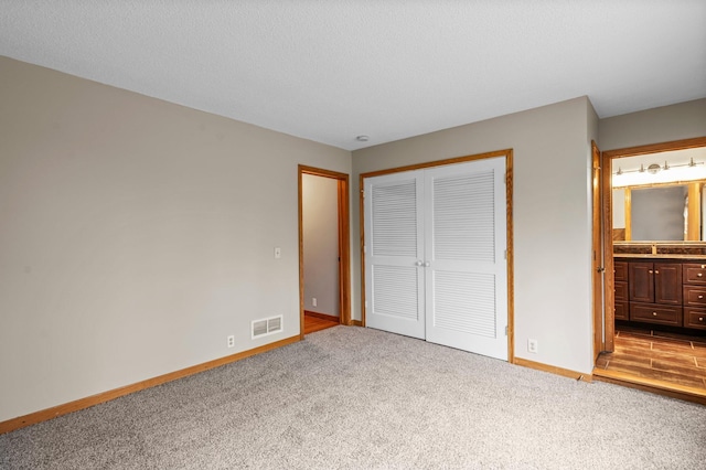 unfurnished bedroom featuring a textured ceiling, light colored carpet, ensuite bath, and a closet